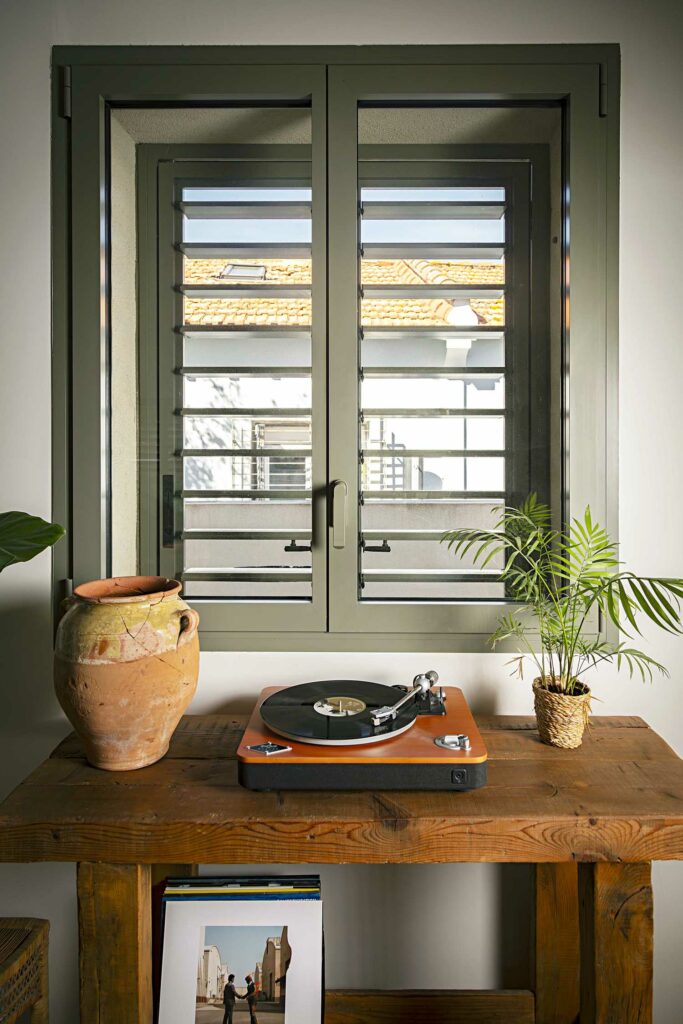 Double porte fenêtre volets intérieurs horizontaux blancs, cadre vert foncé, intérieur épuré, table basse design
