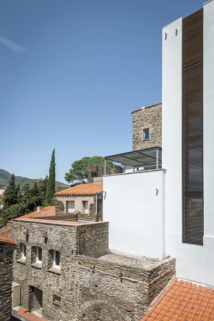 Extension architecturale contemporaine volets bois horizontaux, mur pierre blanche, intégration maison ancienne, paysage méditerranéen