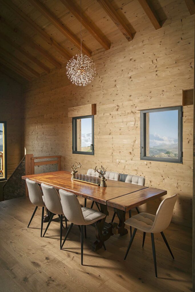 Salle à manger chalet, fenêtres cintrées bois chauffé, poutres apparentes, vue paysage alpin