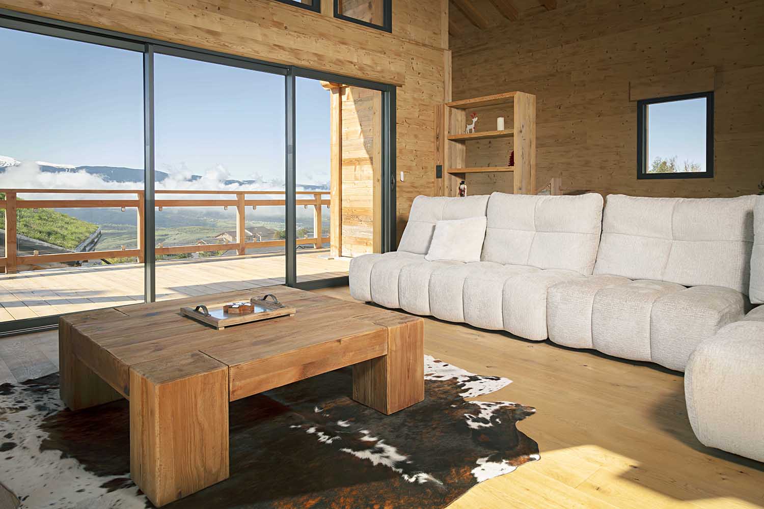 Baie vitrée coulissante panoramique chalet luxe, montagnes enneigées, canapé blanc, vitrage teinté