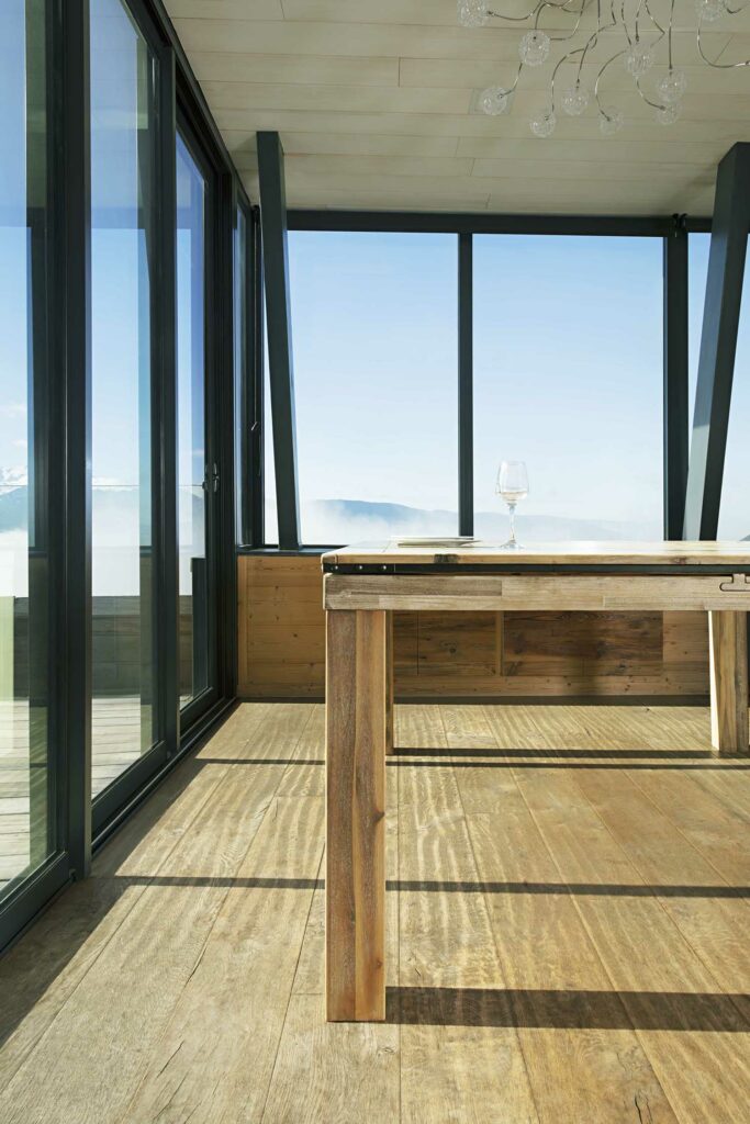 Véranda spacieuse avec grande baie vitrée et table en bois massif, vue montagne, lustre design, plafond bois clair